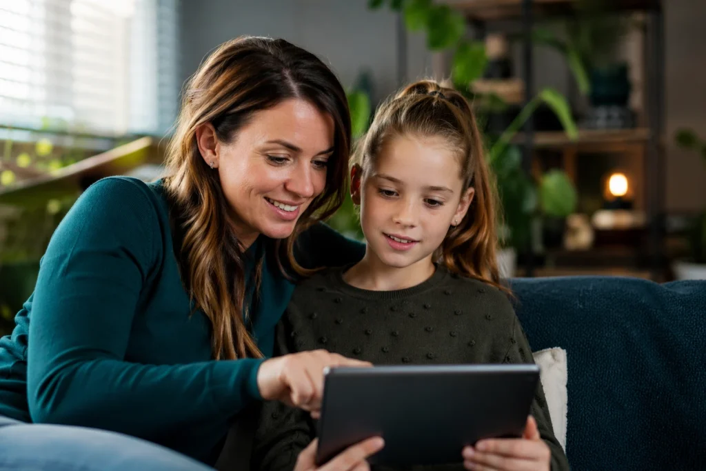 Moeder en dochter kijken samen lachend naar een tablet op de bank